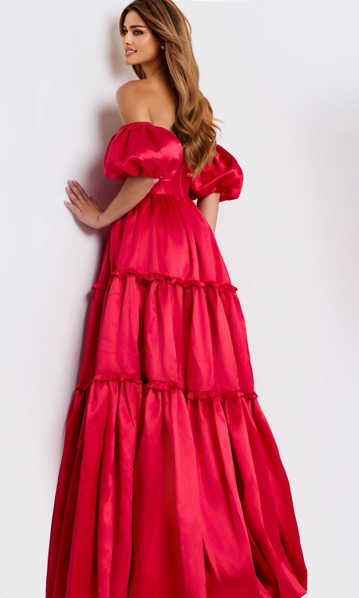 A woman models the Jovani 49055 long prom dressโa bright pink, off-the-shoulder satin gown with a tiered skirtโstanding against a white background and looking to her left.